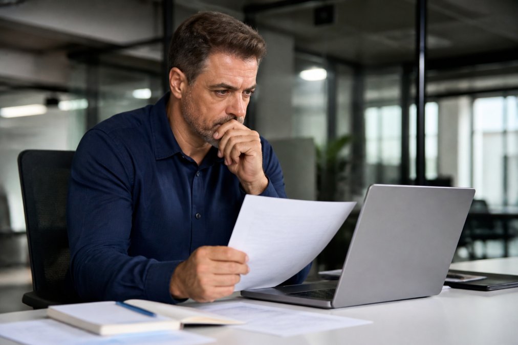 Hiring manager looking concerned while reviewing background checks on a laptop in a modern office